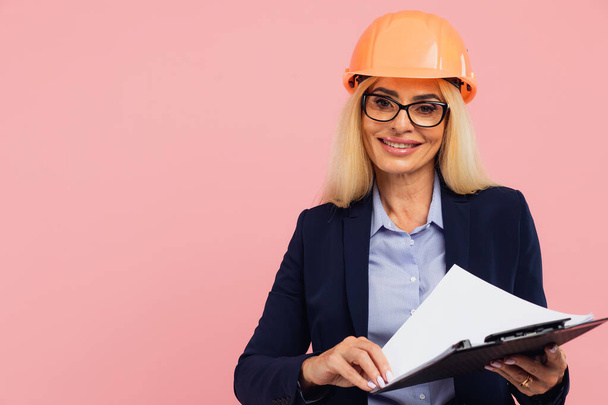 Ritratto di attraente donna d'affari matura architetto o ingegnere in occhiali uso cartella con documenti sullo sfondo rosa - Foto, immagini