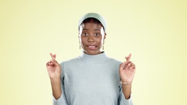 Zwarte vrouw, vingers gekruist en hoop in studio met handen of gezicht emoji op gele achtergrond. Portret van moslim meisje hand teken voor wens, bezorgd of angstig voor loterij wedstrijd prijs of weggeven. - Video