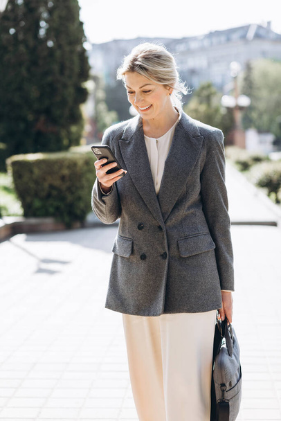 Mature blond smiling business woman walks the streets of the city and communicates by video call - Photo, Image