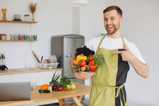 Onnellisen miehen muotokuva, jolla on lautasellinen tuoreita vihanneksia keittiön taustalla kotona - Valokuva, kuva