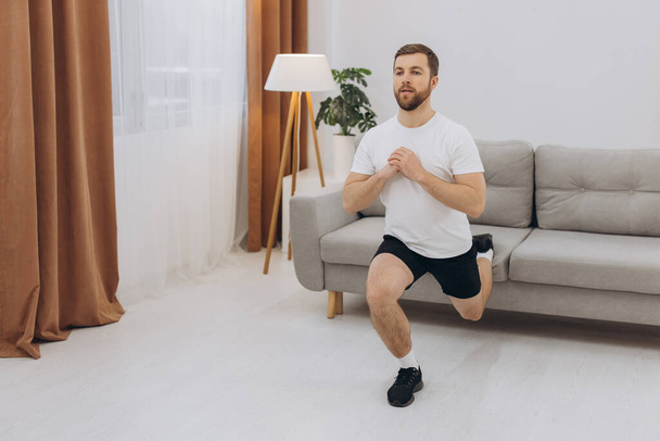 Positive athletic bearded middle-aged man stretching at home, using laptop, watching sport videos on Internet, having fitness class online, copy space. Healthy lifestyle, sport on self-isolation - Foto, imagen