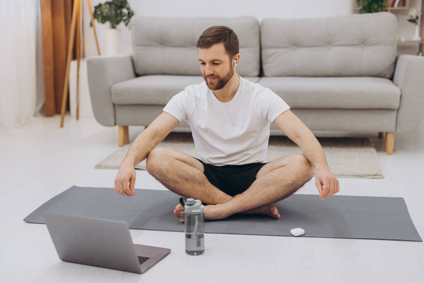 Mantenham a calma em quarentena. Millennial cara meditando com treinador on-line via conexão laptop, espaço vazio
 - Foto, Imagem