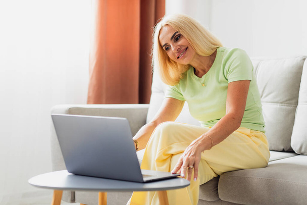 Attraente donna bionda di mezza età utilizza laptop e videochiamate - Foto, immagini