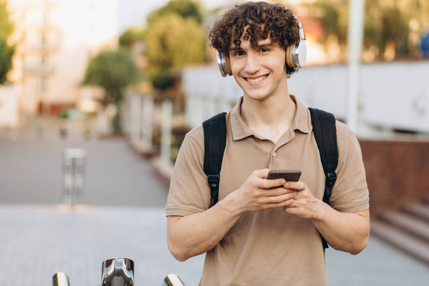 Atractivo joven rizado universitario o estudiante universitario con teléfono caminando por el campus - Foto, Imagen