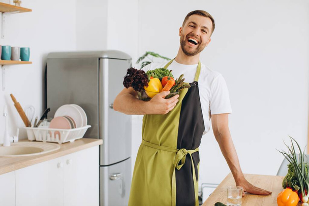 Πορτρέτο ενός ευτυχισμένου άνδρα κρατώντας ένα πιάτο φρέσκα λαχανικά στην κουζίνα - Φωτογραφία, εικόνα