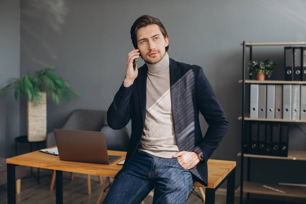 Όμορφος επιχειρηματίας με κοστούμι μιλάει στο τηλέφωνο στο σύγχρονο γραφείο - Φωτογραφία, εικόνα