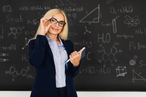 Portret van een vrolijke blonde lerares in de buurt van het schoolbord in de klas. - Foto, afbeelding