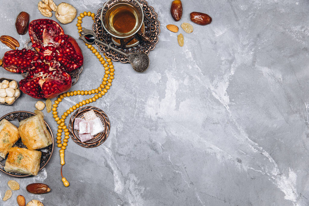 Стильный баннер с традиционной арабской посудой и наборы продуктов питания, чашка чая, Коран и четки на сером фоне камня. Вид на таблицу Рамадана - Фото, изображение