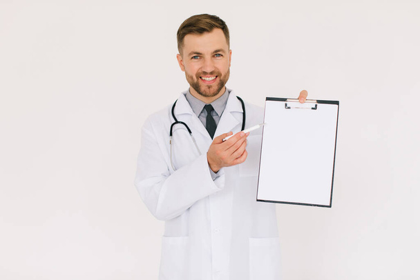 Ευτυχής αρσενικό γιατρό με ένα φάκελο δείχνει κάτι στο χώρο αντίγραφο σε λευκό φόντο - Φωτογραφία, εικόνα