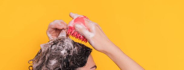 Lady with foam on her head takes care of her scalp with pink massager against yellow background. - Foto, afbeelding