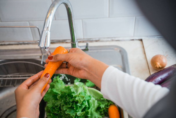 close up of womans hand washing carrots with running water in the sink - Valokuva, kuva