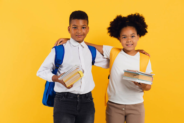 Feliz colegiala afroamericana y colegial de raza mixta sosteniendo libros sobre fondo amarillo, espacio para copiar. - Foto, imagen