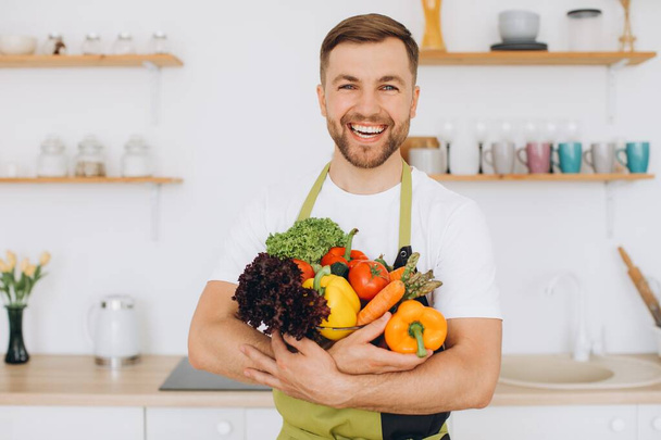 Muotokuva onnellinen mies pitää lautasellinen tuoreita vihanneksia keittiössä - Valokuva, kuva