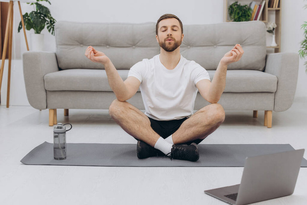 Mantenham a calma em quarentena. Millennial cara meditando com treinador on-line via conexão laptop, espaço vazio
 - Foto, Imagem