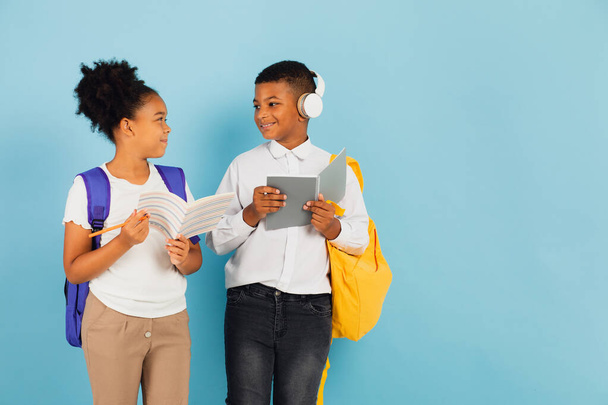 Mieszany uczeń rasy mieszanej i afroamerykańska uczennica czytają razem zarys w klasie szkolnej na niebieskim tle, z powrotem do koncepcji szkoły. - Zdjęcie, obraz