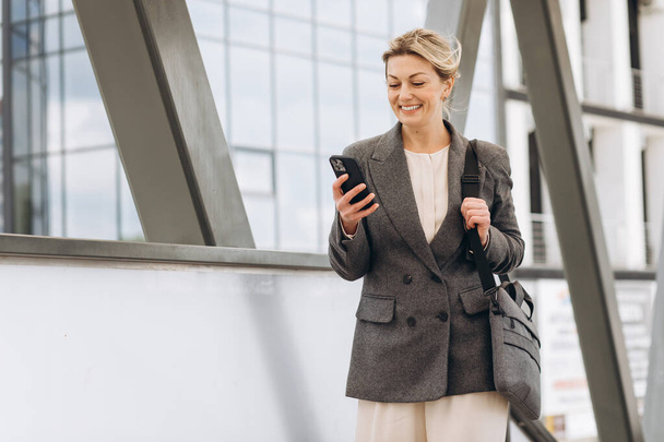 Muotokuva kaunis kypsä liiketoiminnan nainen puku ja harmaa takki hymyilee ja puhuu puhelimessa modernilla kaupunkitausta - Valokuva, kuva