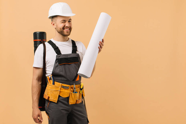 Pozitivní konstruktér zkoumá výkres a drží trubici na béžovém pozadí - Fotografie, Obrázek