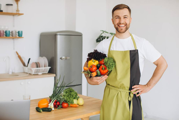 Egy boldog ember portréja, aki friss zöldségeket tart otthon a konyha hátterében. - Fotó, kép