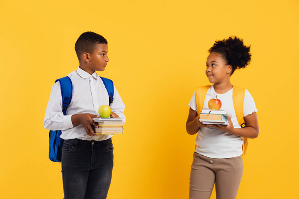 Feliz estudante afro-americana e mista estudante segurando livros em fundo amarelo, espaço de cópia. - Foto, Imagem