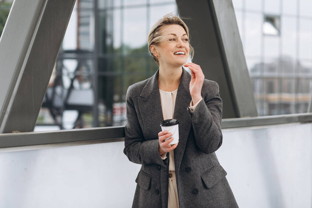 Portrait of a mature business woman smiling with emotions and drinking coffee on the modern urban background - Fotografie, Obrázek