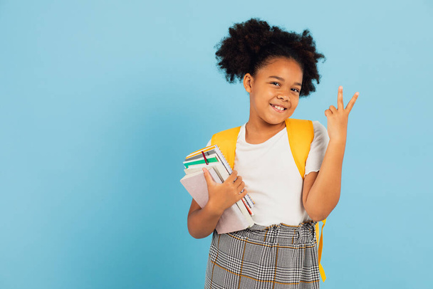 幸せなアフリカ系アメリカ人の女子高生が青い背景を指差して学校のコンセプトに戻る. - 写真・画像