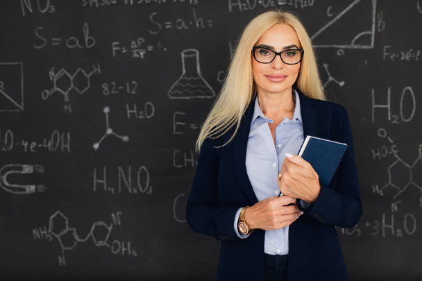 Portret szczęśliwej blondynki nauczycielki stojącej przy tablicy w klasie. - Zdjęcie, obraz