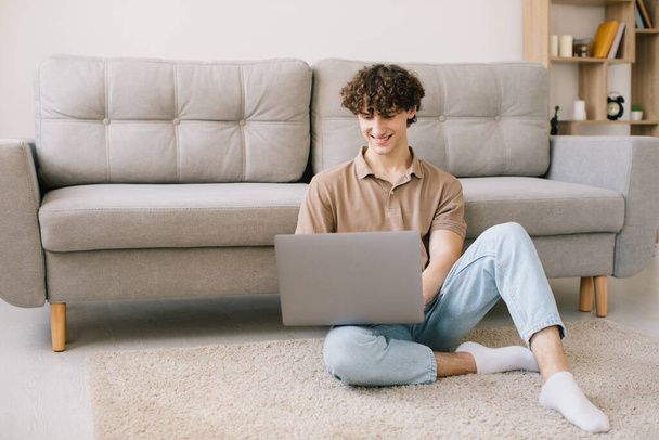 Portrait of attractive young curly hair man using laptop while sitting on sofa at home - Foto, afbeelding