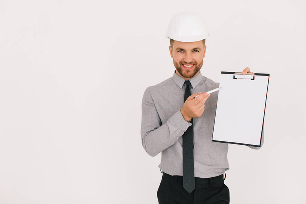 Feliz arquitecto jefe masculino sosteniendo una carpeta con espacio de copia y mostrando algo sobre un fondo blanco - Foto, imagen