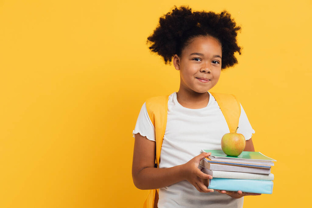 gelukkig Afrikaans amerikaans schoolmeisje met notebooks en boeken over gele achtergrond, kopiëren ruimte. - Foto, afbeelding