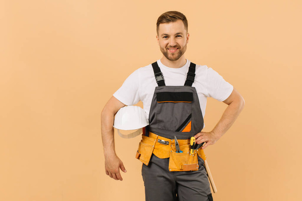 Hombre trabajador de la construcción sosteniendo un casco sobre un fondo beige - Foto, imagen