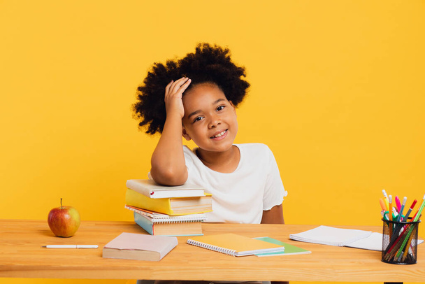 Szczęśliwa Afroamerykanka odrabiająca lekcje siedząc za biurkiem. Powrót do koncepcji szkoły. - Zdjęcie, obraz