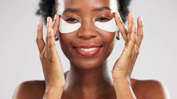 Face, skincare and happy black woman with eye mask in studio isolated on a gray background. Dermatology portrait, beauty cosmetics and female model pose with facial collagen patches for healthy skin - Footage, Video