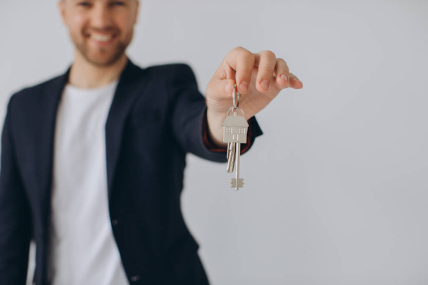 Porträt des fröhlichen professionellen Immobilienmaklers, der Klemmbrett hält und Schlüssel in der Hand zeigt, selektiver Fokus. - Foto, Bild