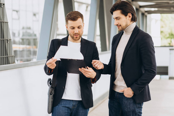 Due uomini d'affari felici moderni con documenti che discutono qualcosa sullo sfondo di uffici urbani ed edifici - Foto, immagini