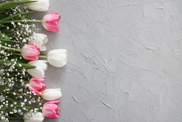 Pink tulips and white gypsophila flowers bouquet on a stylish gray stone background. Mothers Day, birthday celebration concept. Copy space for text. Mockup - Photo, image