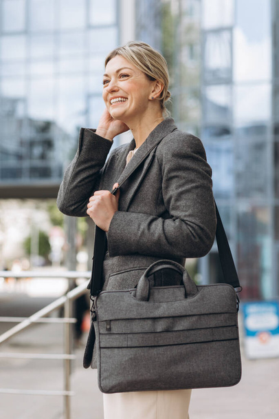 Πορτρέτο μιας ώριμης επιχειρηματία χαμογελώντας με συναισθήματα σε ένα σύγχρονο γραφείο και αστικό υπόβαθρο - Φωτογραφία, εικόνα
