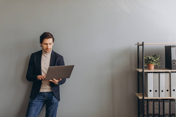 Imagem de homem de negócios alegre jovem em terno que mantém e usa o computador portátil no escritório moderno - Foto, Imagem