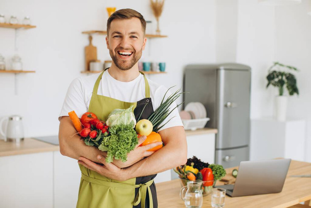 Hombre feliz sosteniendo muchas verduras frescas diferentes en la cocina en casa - Foto, imagen