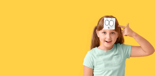 Šťastná holčička s překvapeným emotikonu na čele proti žluté pozadí s prostorem pro text - Fotografie, Obrázek