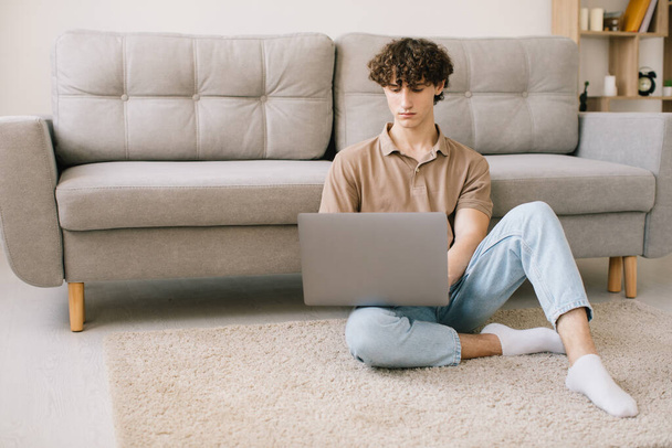 Portrait of attractive young curly hair man using laptop while sitting on sofa at home - Fotó, kép