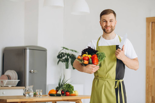 Портрет щасливого чоловіка, який тримає тарілку зі свіжих овочів на фоні кухні вдома
 - Фото, зображення