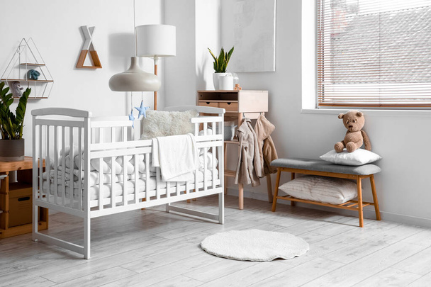 Interior of light children's bedroom with baby crib, table and bench - Фото, изображение