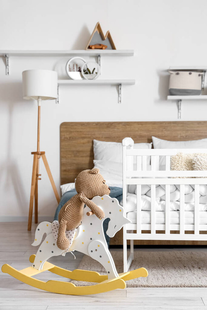 Interior of light bedroom with bed, baby crib and toys - Foto, afbeelding