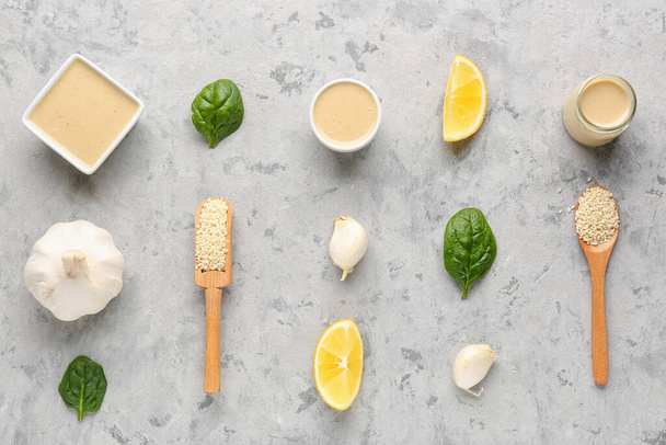 Composition with tasty tahini, sesame seeds, garlic, spinach and lemon slices on grunge background - Foto, imagen