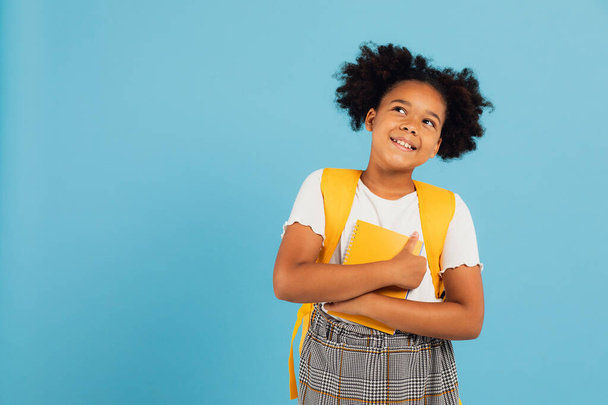 Happy African American schoolgirl holding books on blue background, back to school concept. - Foto, imagen