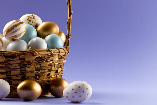 Image of multi coloured easter eggs in basket and copy space on purple background. Easter, religion, tradition and celebration concept. - Фото, изображение