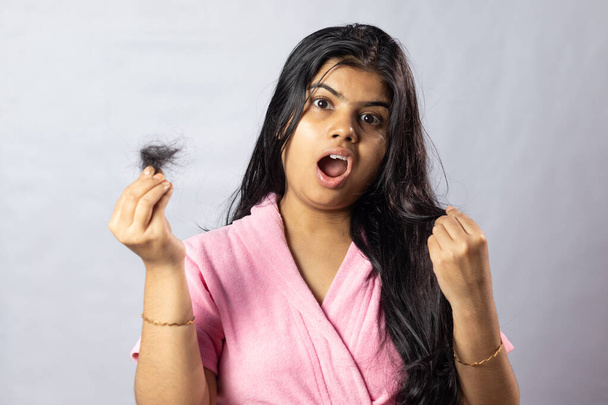 Ein besorgtes indisches Mädchen im rosafarbenen Bademantel mit Haarfallproblem auf weißem Hintergrund - Foto, Bild