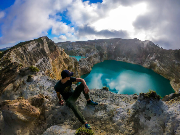 Man sitting at the volcano rim and watching the Kelimutu volcanic crater lakes in Moni, Flores, Indonesia. Man is relaxed and calm, enjoying the view on lake shining with many shades of turquoise - Foto, Imagen