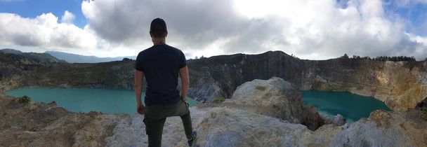 Hombre parado en el borde del volcán y observando los lagos del cráter volcánico Kelimutu en Moni, Flores, Indonesia. El hombre está relajado y tranquilo, disfrutando de la vista de los lagos turquesas. Los lagos tienen diferentes colores - Foto, imagen
