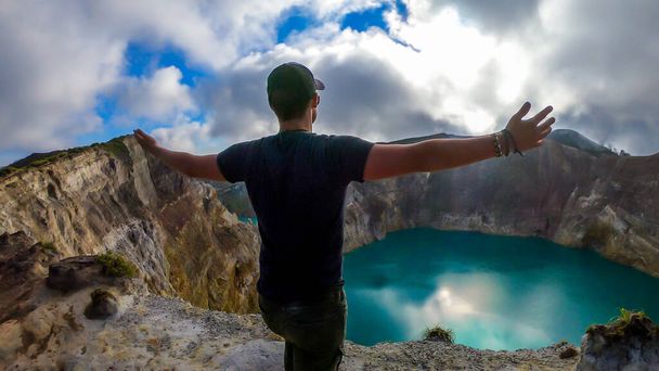 Man standing at the volcano rim with arms spread and watching the Kelimutu volcanic crater lakes in Moni, Flores, Indonesia. Man engages with life and has the feeling of freedom - Foto, Imagen